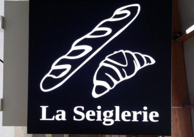 Vos enseignes à Lyon: Caisson drapeau à Grigny (Rhône), de 800 x 800 mm, en aluminium 30/10ème laqué noir mât, ajouré des 2 faces , avec un contre-collage en PMMA blanc diffusant 3 mm, éclairage led pour la Seiglerie ( 42320 La Grand Croix )